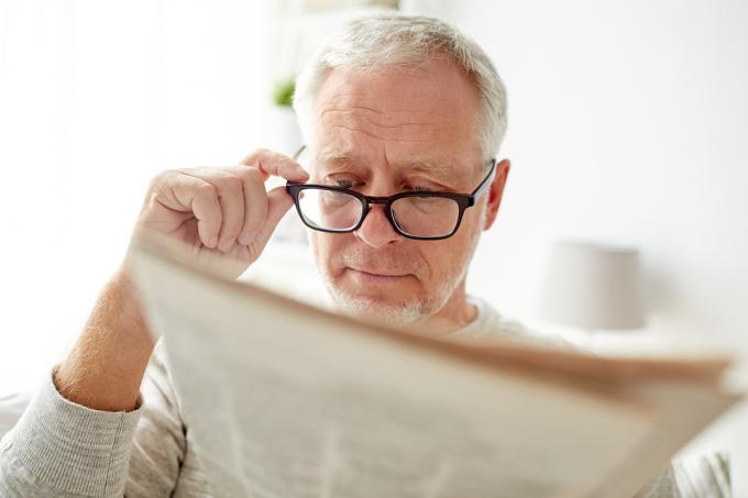גבר בכיר במשקפיים קורא עיתון בבית