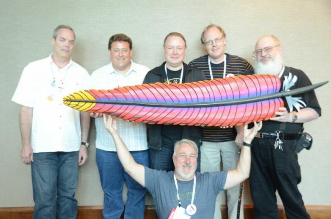 Skupina mužov drží pierko s logom nadácie Apache Software Foundation.